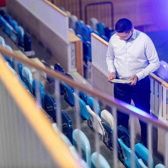 Mann steht mit Klemmbrett zwischen einer Reihe Stühlen