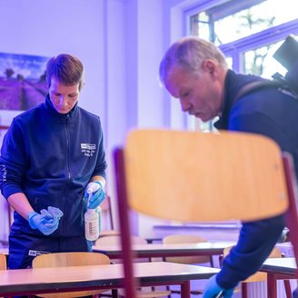 zwei Personen, die in einem Klassenzimmer die Tische reinigen