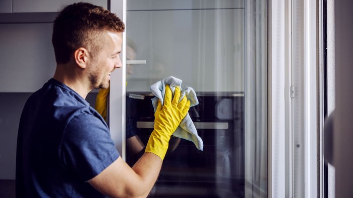 Man, welcher mit einem gelben Tuch Fenster putzt